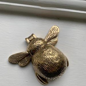 May include: A gold-toned metal bee door knocker with detailed wings and a textured body.