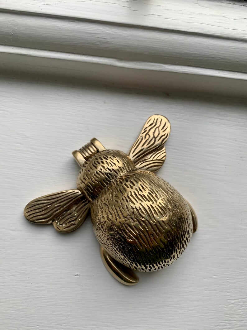 May include: A gold-toned metal bee door knocker with detailed wings and a textured body.