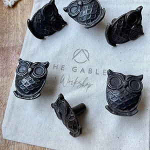 May include: Six black metal owl drawer pulls with a rustic finish. The pulls are arranged on a white canvas bag with the text "The Gable Workshop" printed on it.