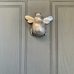May include: A silver bee-shaped door knocker on a gray wooden door.