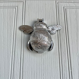 May include: A silver bee-shaped door knocker with textured wings and body.