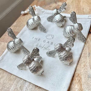 May include: Six silver bee-shaped drawer pulls in a white fabric bag. The bag has the text "The Gable Workshop" printed on it.