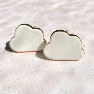 May include: Two white cloud-shaped cabinet knobs with gold trim. The knobs have a smooth, glossy finish and a small gold screw for attachment. The knobs are designed for furniture and home decor.