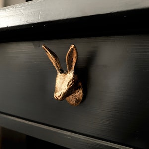 May include: A gold-coloured rabbit head drawer pull on a black painted drawer.
