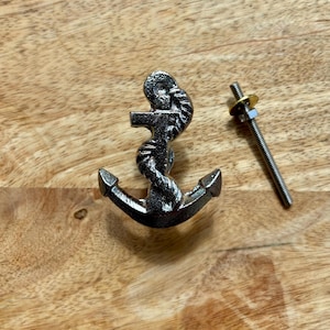 May include: A dark metallic anchor-shaped cabinet knob with a detailed rope design. The nautical-themed hardware includes a threaded bolt for fitting. The cabinet knob is shown on a wooden surface.