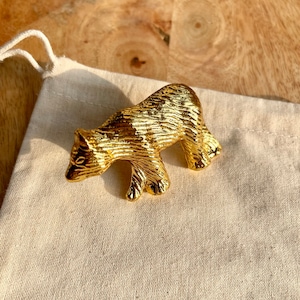 May include: A gold-coloured metal bear figurine. The bear is walking and has a textured surface.