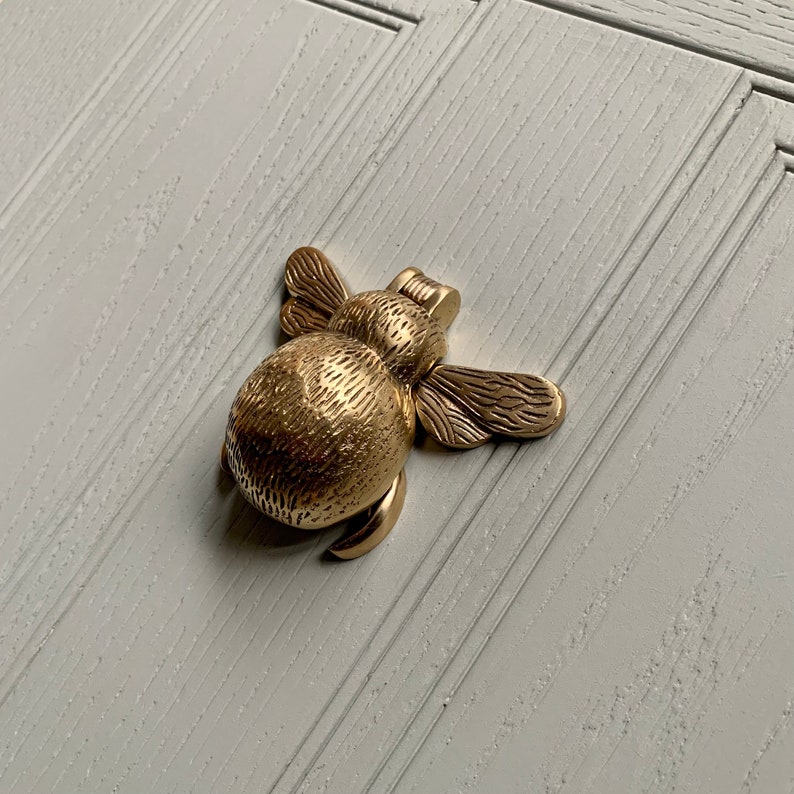 May include: A gold-toned bee-shaped door knocker with a textured body and detailed wings.