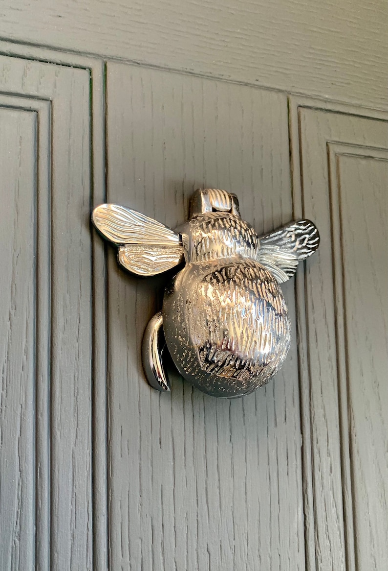 May include: A silver bee-shaped door knocker with detailed wings and a textured body.