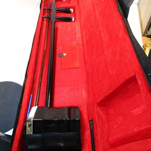 Può includere: Un erhu nero, un tradizionale strumento musicale cinese ad arco a due corde, è all'interno della sua custodia nera aperta. La custodia ha una fodera in velluto rosso brillante.