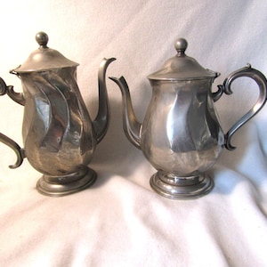 May include: Two silver teapots with a wavy design. The teapots have a classic shape with a spout and handle.