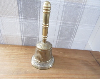 May include: A gold-colored brass bell with a decorative handle. The bell has a ribbed design and intricate floral patterns.