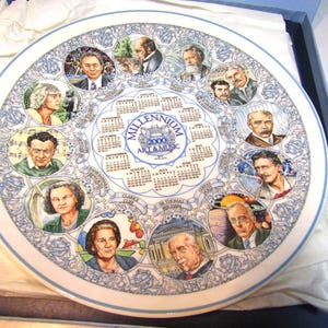 May include: A decorative plate with a blue and white floral border. The center features portraits of historical figures and a calendar for the year 2000, with the text "Millennium 2000 Art & Music". The plate is in a blue box.