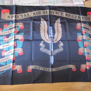 May include: Black flag with the text "SPECIAL AIR SERVICE REGIMENT" and the motto "WHO DARES WINS." The flag features a winged dagger emblem and lists various locations and dates, including Northern Ireland and the Falkland Islands.