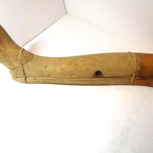 May include: A vintage wooden shoe last, showing the shape of a foot and lower leg. The wood has a light, natural color with darker areas and a small hole. The last is secured with thin bands.