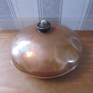 May include: A copper-colored, round, metal oil lamp with a wick and a black cap. The lamp is sitting on a wooden surface.
