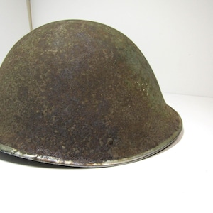 May include: A vintage Brodie-style military helmet featuring a dome-shaped crown and a wide, downward-sloping brim. The exterior surface displays a heavily weathered, rusted brown and green patina with visible metal texture and a metallic rim.