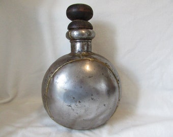 Könnte beinhalten: Eine silberne Metallflasche mit rundem Körper und einem Holzdeckel. Die Flasche hat ein Messingband um die Mitte.