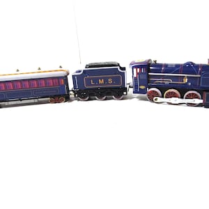 May include: A vintage toy train set featuring a blue locomotive, a coal car, and a passenger car. The locomotive has red wheels and gold accents. The passenger car has red and purple windows. The train set is on a white background.
