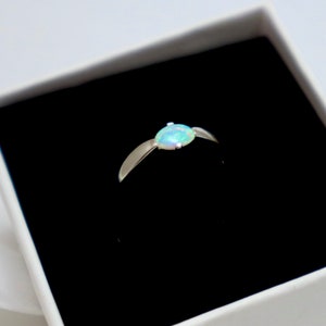 May include: A silver ring with a white opal gemstone. The ring is in a black velvet box.