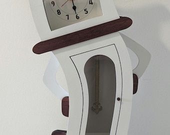 May include: A white and brown wooden clock with a pendulum. The clock is shaped like a person and has a face with Roman numerals. The clock is standing on a table.