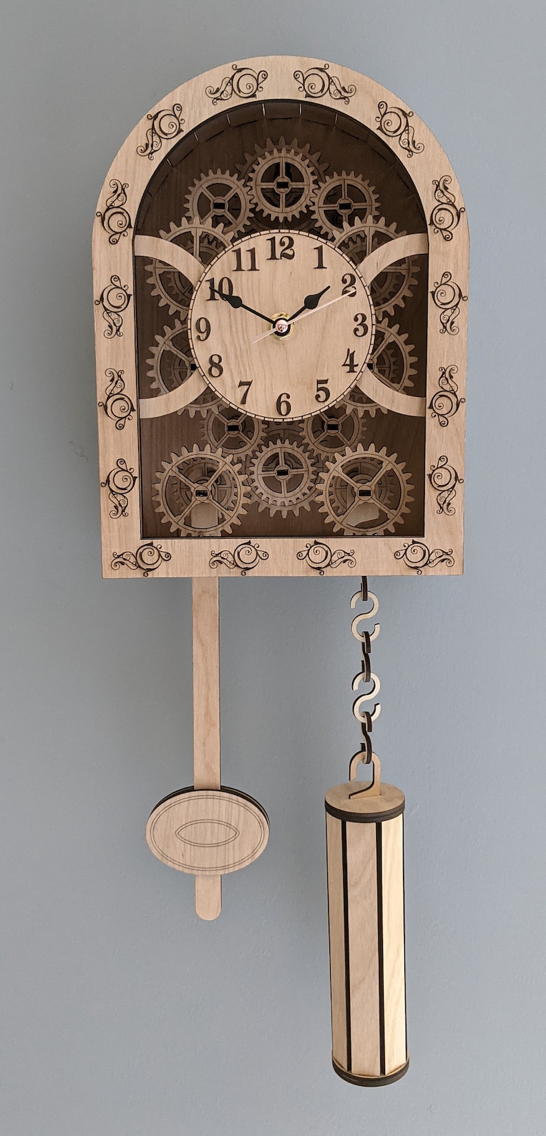 May include: A wooden clock with a pendulum and a face with Roman numerals. The clock has a decorative design with intricate details and gears.