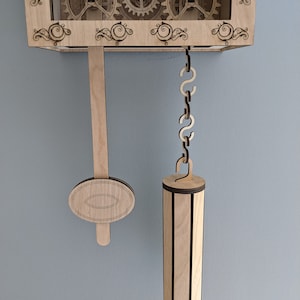 May include: A wooden clock with a pendulum and weights. The clock has a decorative design with gears and scrolls. The pendulum is made of wood and has a round weight at the bottom. The weights are also made of wood and have a cylindrical shape.