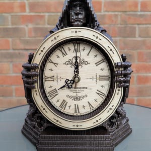 May include: A dark brown, hooded, skeletal-themed clock with a light-coloured circular face featuring black Roman numerals, ornate hands, and the text THE TIMEKEEPER TEMPUS FUGIT. The clock is framed by two dark, claw-like hands on either side.