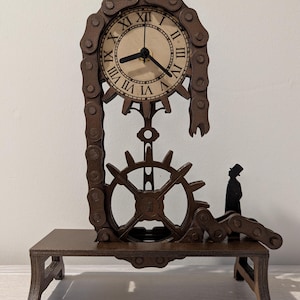 Peut inclure: Une horloge en bois marron avec un design steampunk. Le cadran de l'horloge comporte des chiffres romains et est entouré d'une chaîne. Un engrenage et une petite figurine font également partie du design. L'horloge est posée sur une petite table.