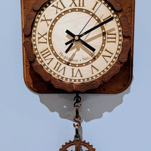 May include: A square wooden wall clock with a light-colored face and Roman numerals. The clock features a decorative chain around the face and a gear-shaped pendulum. The clock reads "Regulator No. 2".