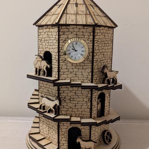 Può includere: Un orologio a torre in legno con una facciata in stile pietra, con un quadrante con numeri romani. Capre in miniatura sono collocate sui balconi della torre. La torre dell'orologio ha un tetto in legno e un ingranaggio alla base.