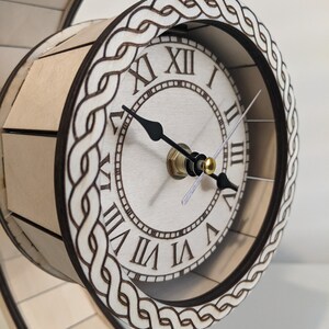 May include: A wooden clock with Roman numeral markings on a white face. The clock is mounted on a curved wooden base with a Celtic knot design.