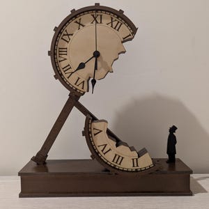 Può includere: Una scultura di orologio in legno marrone dal design surreale. Il quadrante è parzialmente rotto, con numeri romani. Una piccola figura con cilindro è in piedi vicino alla base. L'orologio misura circa 30 cm di altezza.