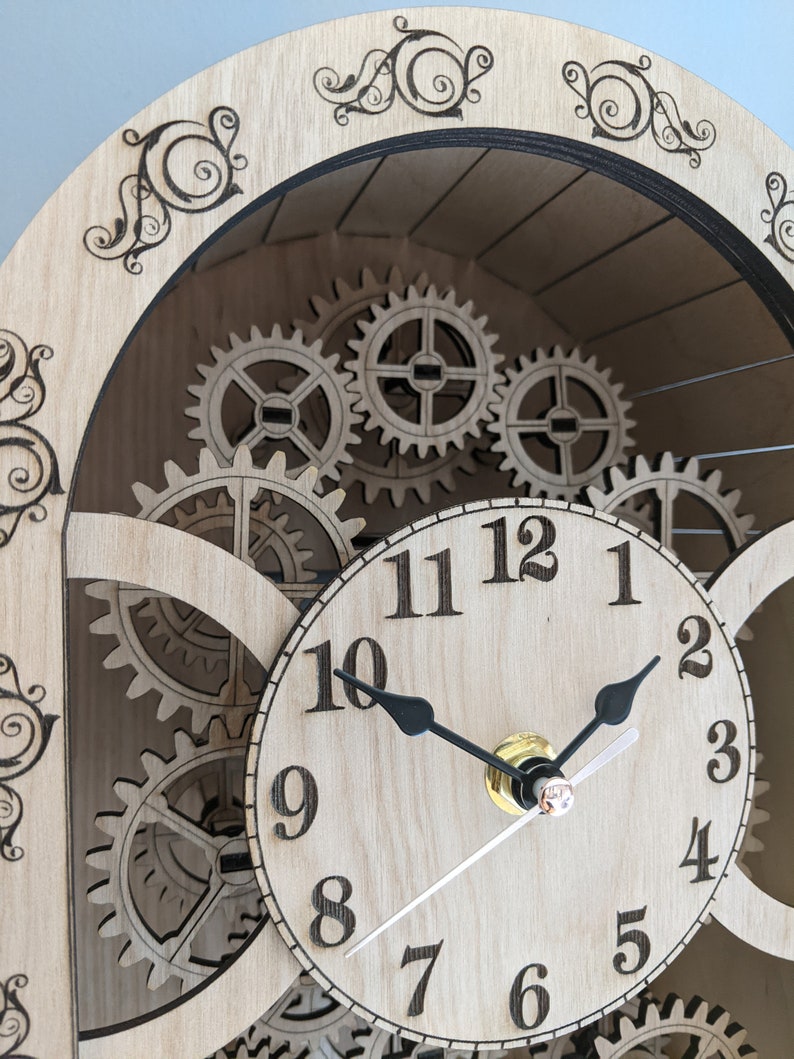 May include: A wooden clock with a circular face and black hands. The clock face has Roman numerals for the hours and Arabic numerals for the minutes. The clock is surrounded by gears, giving it a steampunk aesthetic.