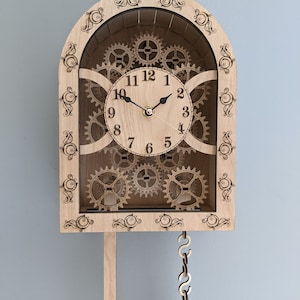 May include: A wooden clock with a pendulum and intricate gears visible behind the clock face. The clock face has Roman numerals and black hands.