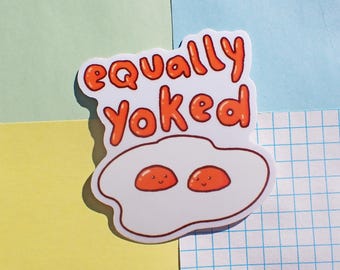 Puede incluir: Pegatina blanca con el texto "equally yoked" en letras naranjas. La pegatina presenta un huevo blanco con dos yemas naranjas con caras sonrientes.
