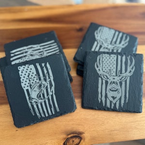 May include: Set of six black slate coasters with an American flag design. Each coaster features a different image, including a deer and a fish.
