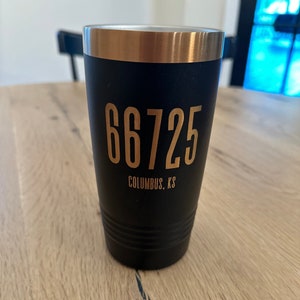 May include: Black and gold travel mug with the text "66725 Columbus, KS" printed on the side.