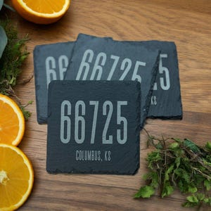 May include: Four black slate coasters with the number 66725 and the text "Columbus, KS" printed in white. The coasters are stacked on top of each other.