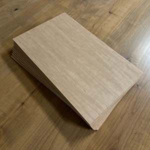 May include: A stack of light brown wood veneer sheets. The sheets are smooth and have a natural wood grain pattern.