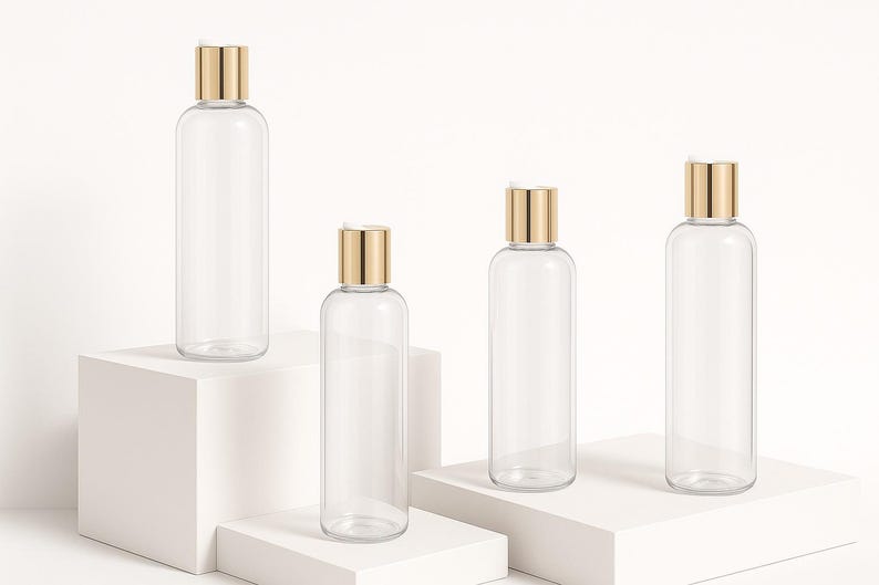 K&ouml;nnte beinhalten: Vier transparente, zylindrische Flaschen mit goldfarbenen Verschl&uuml;ssen werden auf wei&szlig;en geometrischen Plattformen pr&auml;sentiert. Die Flaschen sind leer, was darauf hindeutet, dass sie f&uuml;r Kosmetik- oder K&ouml;rperpflegeprodukte bestimmt sind. Das minimalistische Design und die neutrale Farbpalette schaffen eine saubere, moderne &Auml;sthetik.