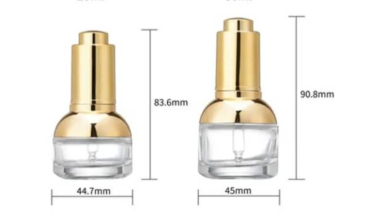 May include: Two clear glass dropper bottles with gold-coloured caps. The bottles are labelled with measurements: 83.6mm and 90.8mm in height, and 44.7mm and 45mm in width. The bottles are designed for cosmetic or skincare products.