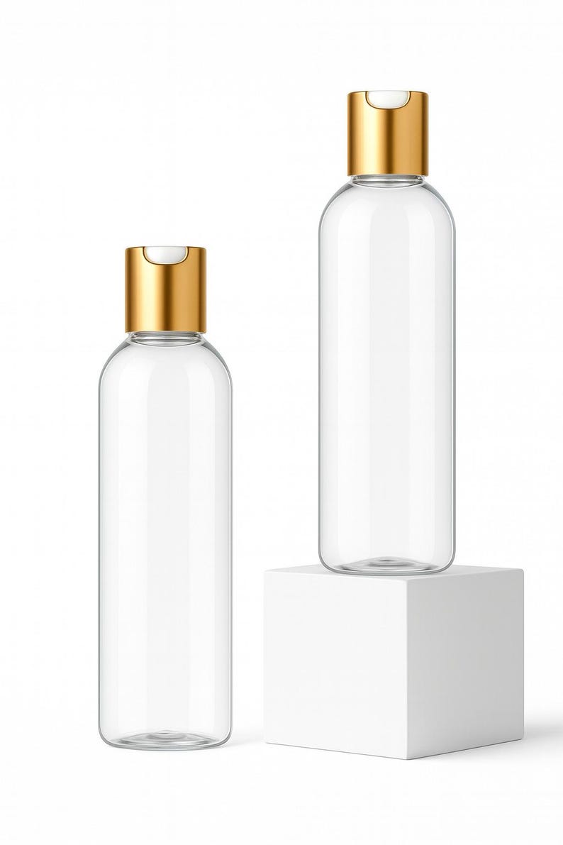 K&ouml;nnte beinhalten: Zwei transparente, zylindrische Flaschen mit goldfarbenen Klappdeckeln. Eine Flasche steht auf einem wei&szlig;en W&uuml;rfel, die andere auf der Oberfl&auml;che. Die Flaschen sind leer und scheinen aus Glas oder klarem Kunststoff zu bestehen.