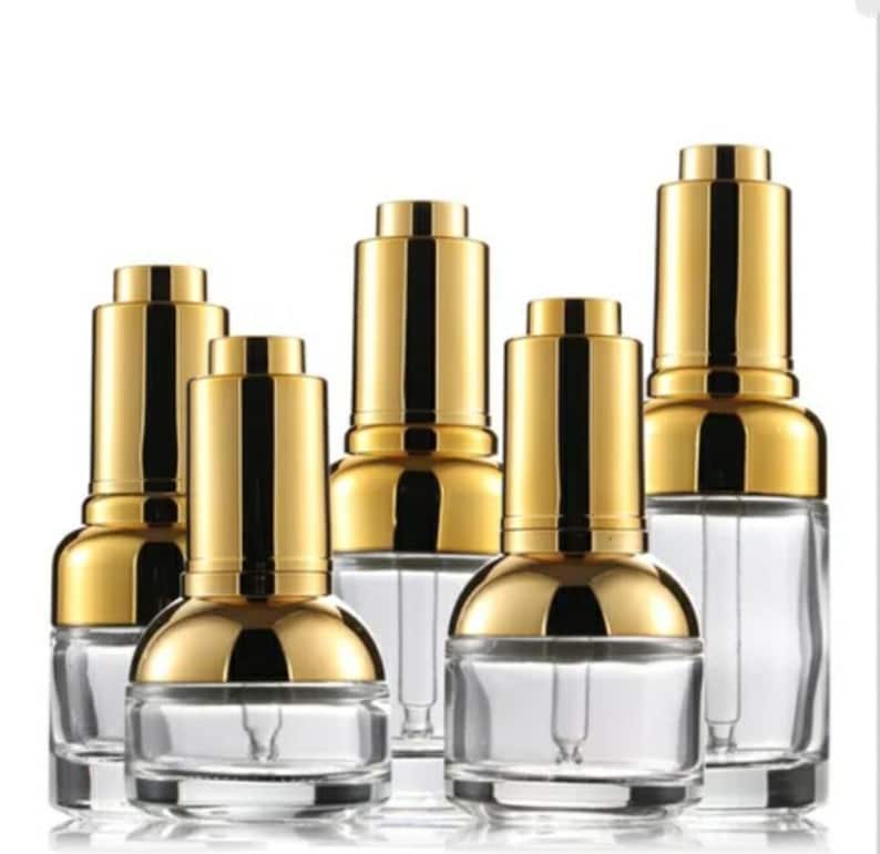 May include: Several clear glass dropper bottles with gold-coloured caps. The bottles have a rounded base and a long, thin dropper inside. The gold caps have a shiny, metallic finish. The bottles are arranged in a group against a white background.
