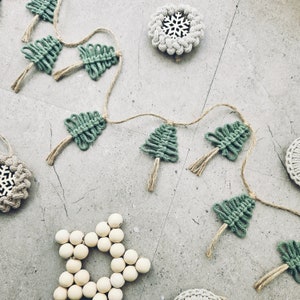 May include: A green and brown macrame garland with a string of small Christmas trees and a wooden star ornament.