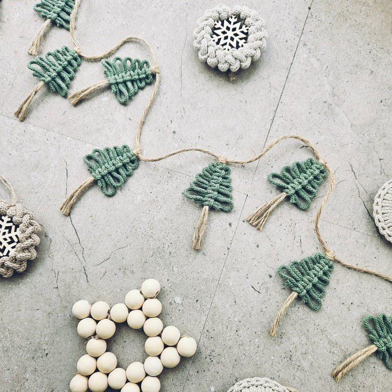 May include: A green and brown macrame garland with a string of small Christmas trees and a wooden star ornament.