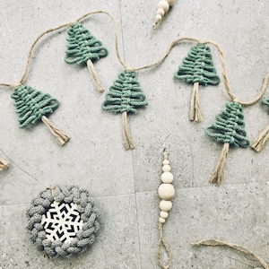 May include: A green and brown string garland with a series of knotted Christmas tree ornaments. The garland is strung with twine and has a wooden bead ornament hanging from it.