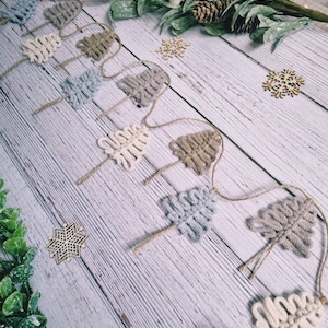 May include: A garland of crocheted Christmas trees in shades of beige, grey, and white. The trees are strung together with twine and are decorated with wooden snowflakes.