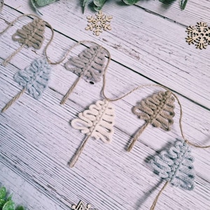 May include: A garland of crocheted Christmas trees in beige, brown, and grey colours. The trees are strung together with twine and are decorated with wooden snowflakes.