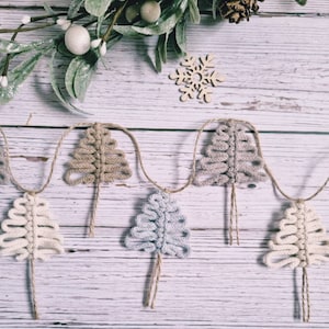 May include: A garland of crocheted Christmas trees in beige, light blue and white, strung on twine against a whitewashed wood background.