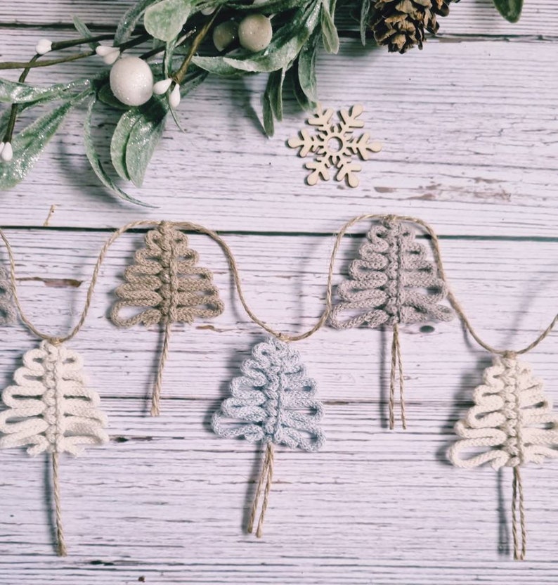May include: A garland of crocheted Christmas trees in beige, light blue and white, strung on twine against a whitewashed wood background.